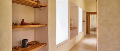 A corridor with wooden shelves on the walls, some with decorative items, and large windows on the right side.