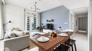 A modern living room with a dining area, a sofa, a TV, and a dining table set with plates and glasses. - 2BR Beachfront Retreat with Palm Views (Dubai)