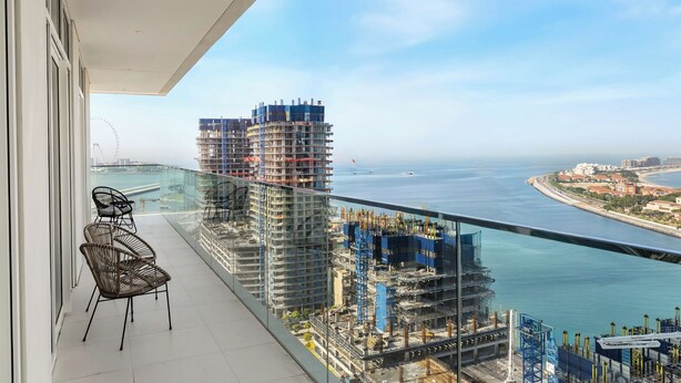A balcony with a view of a coastal cityscape, including a large building under construction and a clear sky. - 2BR Beachfront Retreat with Palm Views (Dubai)