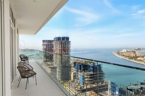 A balcony with a view of a coastal cityscape, including a large building under construction and a clear sky. - 2BR Beachfront Retreat with Palm Views (Dubai)