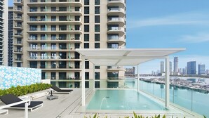 A rooftop pool with a city view, lounge chairs, and a modern building in the background. - 2BR Beachfront Retreat with Palm Views (Dubai)