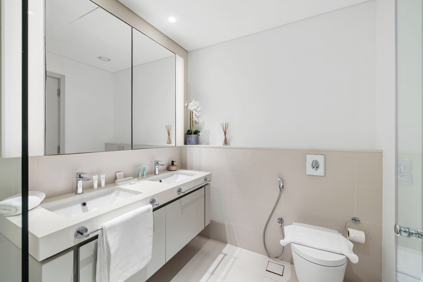 Une salle de bain moderne avec deux lavabos, un grand miroir, des toilettes et une douche.