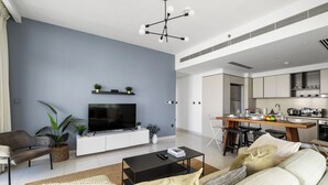A modern living room with a flat-screen TV, a sofa, a coffee table, and a dining area with a kitchen in the background. - 2BR Beachfront Retreat with Palm Views (Dubai)
