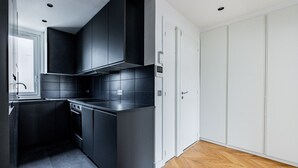 A modern kitchen with dark cabinetry, a built-in oven, and a herringbone-patterned wooden floor. - Two bedroom  in France, Paris (Paris)