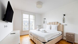 A modern bedroom with a large bed, a TV mounted on the wall, and a window with a view of buildings. - Two bedroom  in France, Paris (Paris)