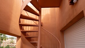 A spiral staircase with a metal railing, leading to a balcony with a view of a residential area.