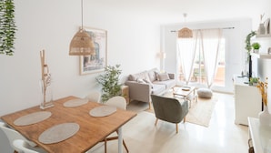 A modern living room with a wooden dining table, white chairs, a grey sofa, and a white cabinet.