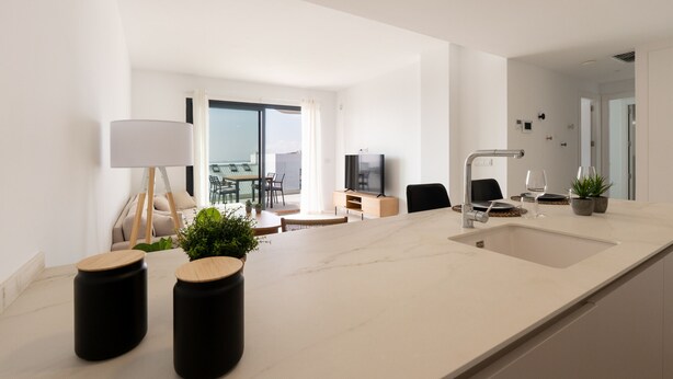 Una cocina moderna con una isla grande, un comedor con mesa y sillas, y una sala de estar con sofá y televisor.