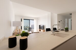 A modern kitchen with a large island, a dining area with a table and chairs, and a living space with a sofa and a TV. - Las Lomas del Higueron - Brand New Apartment (Fuengirola)