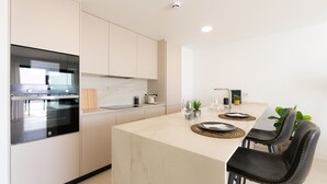 Una cocina moderna con horno integrado, encimera de mármol y comedor con una mesa dispuesta para dos personas.