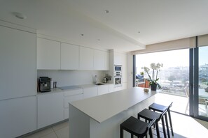 A modern kitchen with white cabinets, a large island with bar stools, and a view of the city through large windows. - Higueron West IX - El Olivo Stylish Deluxe Apart (Fuengirola)