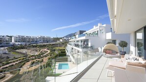 En moderne balkon med gelænder i glas, med udsigt over swimmingpool og anlagt have.