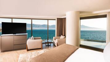 Habitación de hotel con una cama grande, televisión, dos sillones, una mesita y vistas al mar y a las montañas.