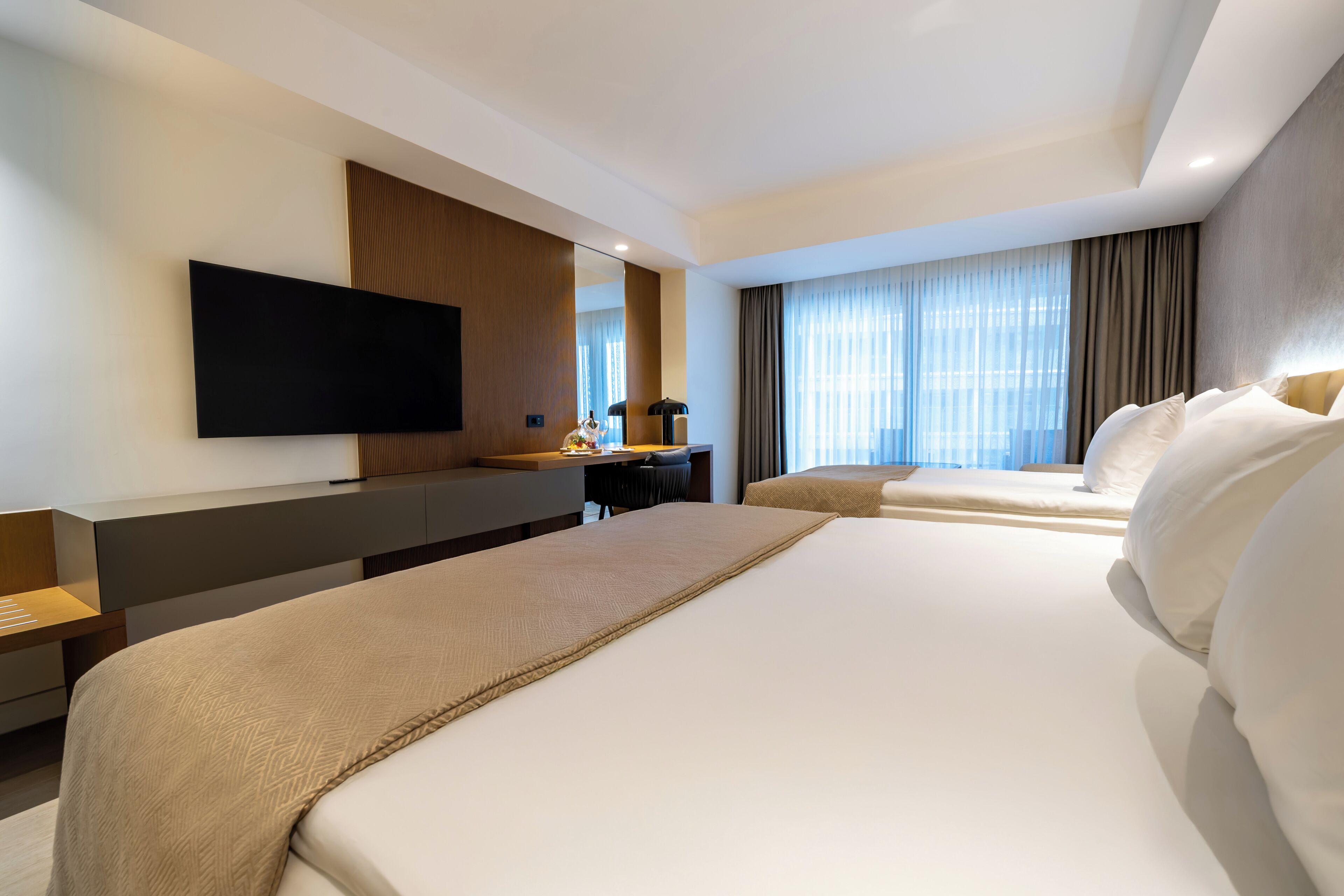 Ein Hotelzimmer mit einem großen Bett, einem Schreibtisch mit Stuhl, einem an der Wand befestigten Flachbildfernseher und einem Fenster mit Vorhängen.