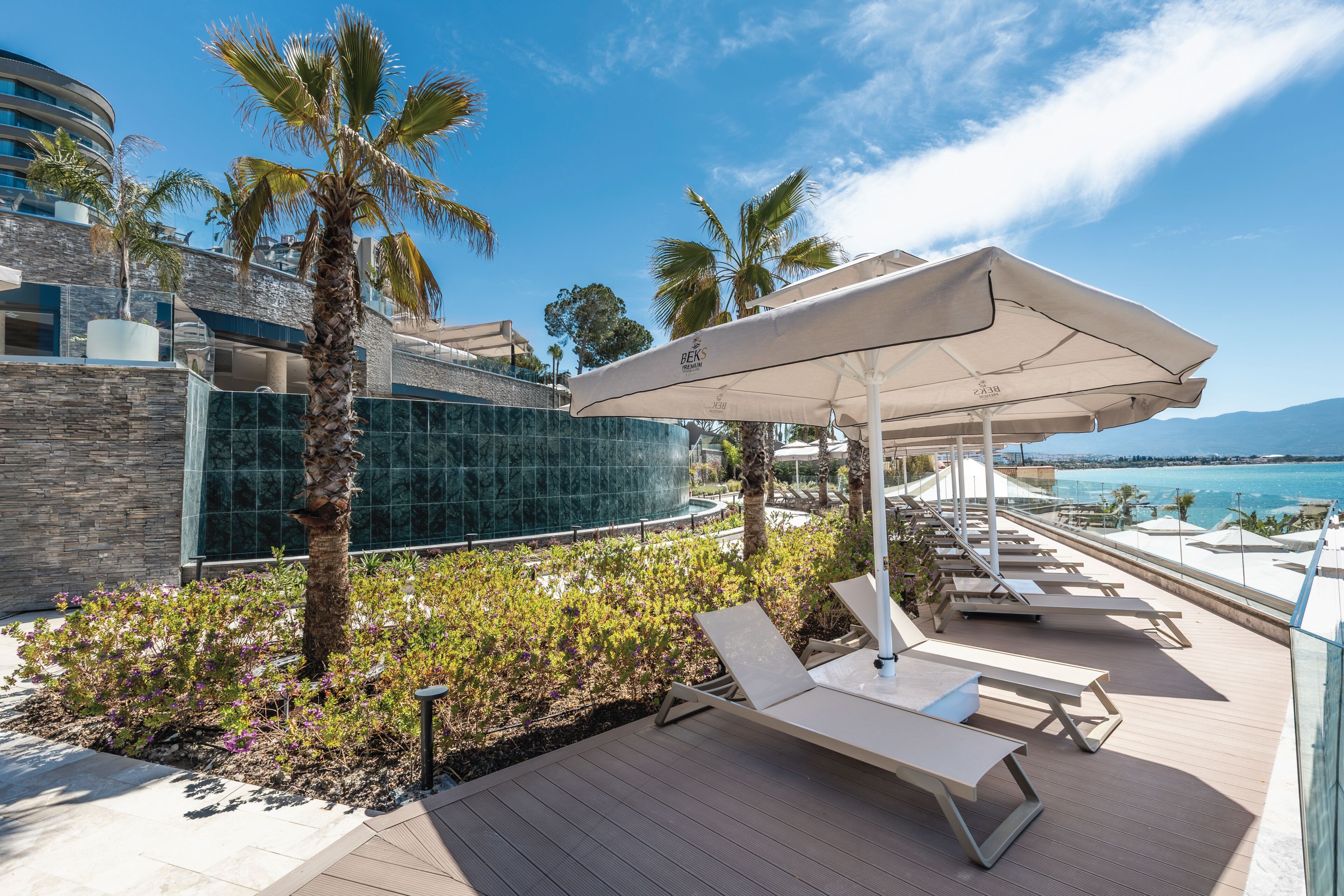 Un espace piscine aménagé sur le toit, avec des chaises longues, des parasols et des palmiers.