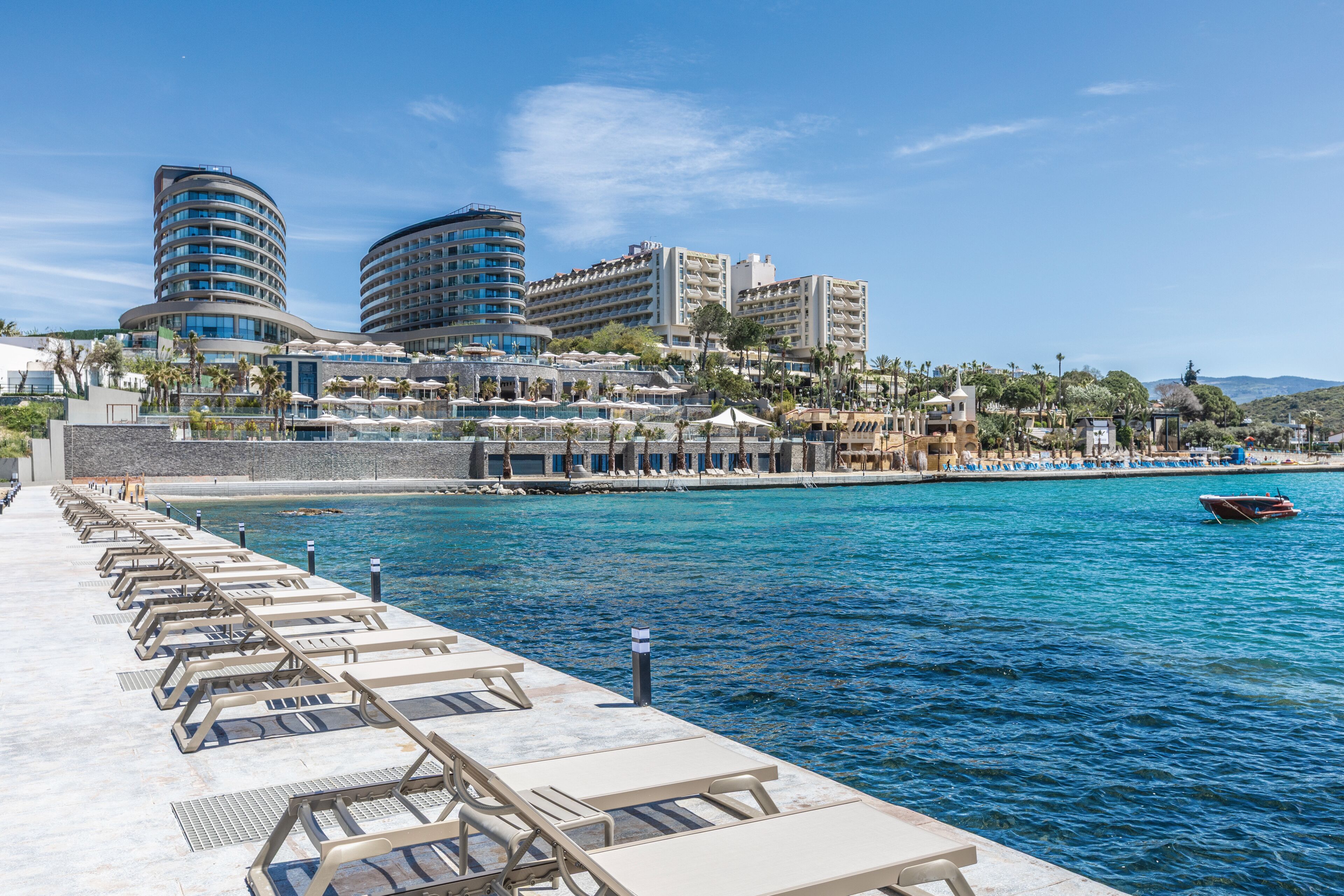 Un hotel frente al agua con zona de lounge junto a la piscina, varias edificaciones del hotel y un muelle para embarcaciones.