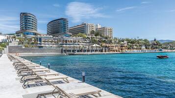 Un hotel frente al agua con zona de lounge junto a la piscina, varias edificaciones del hotel y un muelle para embarcaciones.