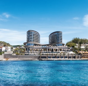 A waterfront hotel with two cylindrical buildings, a pool, and a beach area.