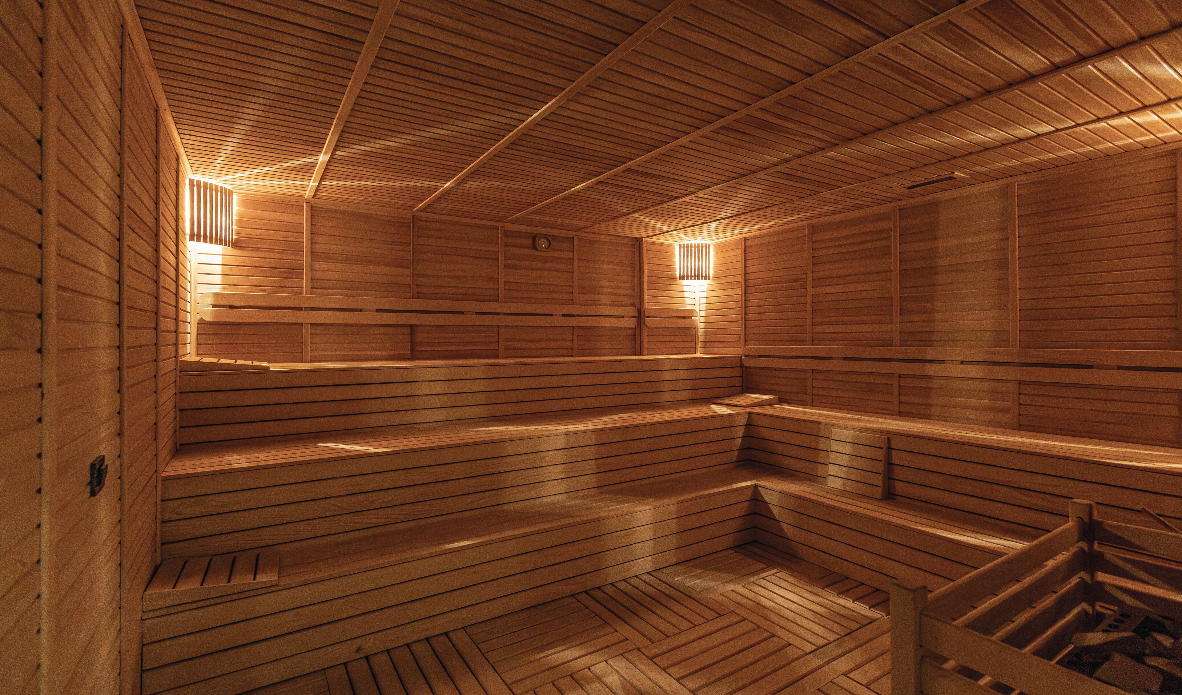 A sauna with wooden benches and walls, and two wall-mounted light fixtures.