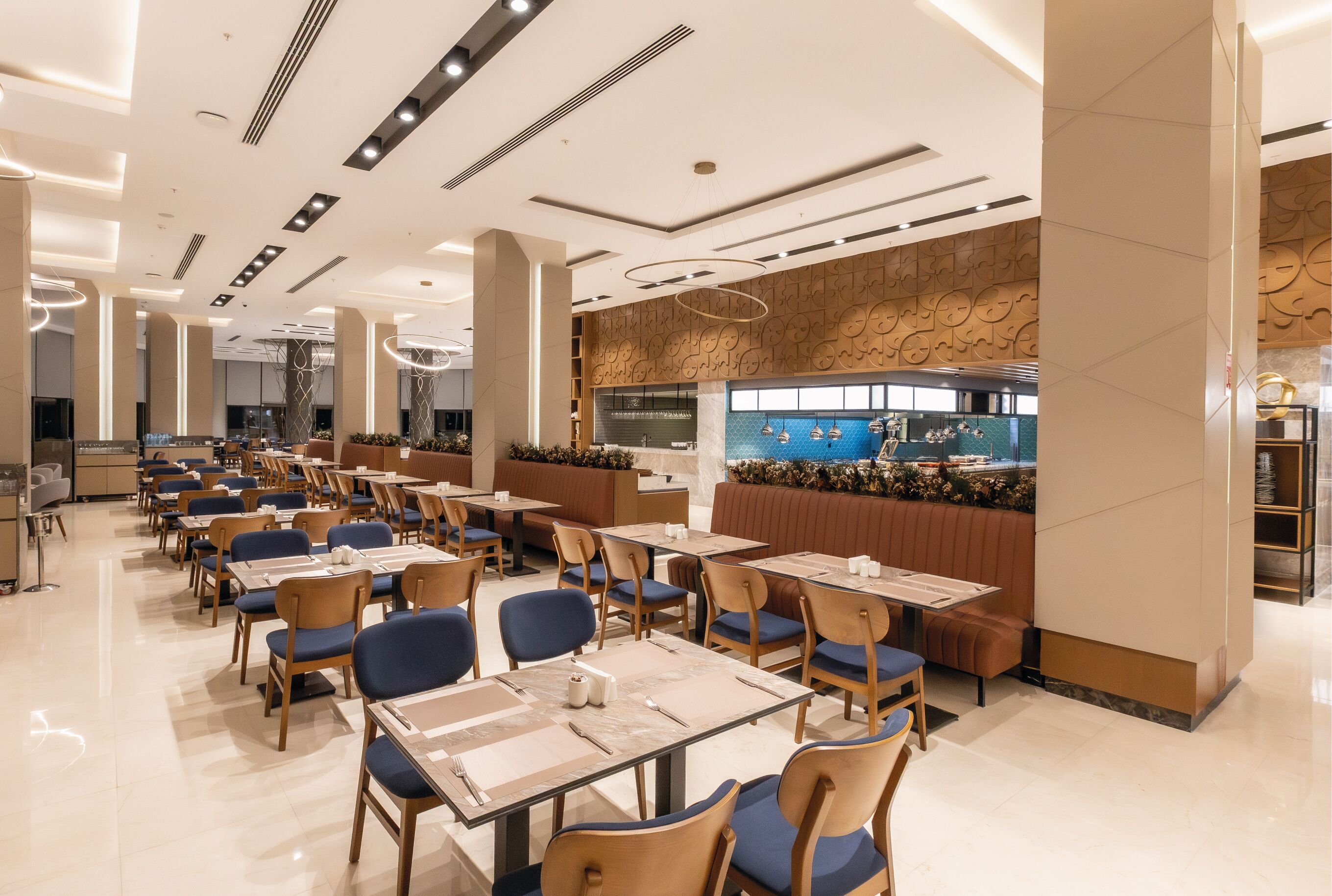 A spacious dining area with multiple tables and chairs, a central bar area, and a decorative wall with a pattern.