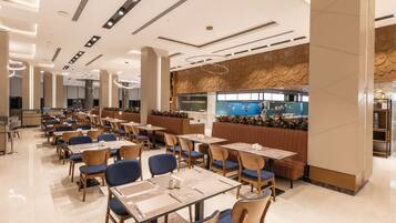 A spacious dining area with multiple tables and chairs, a central bar area, and a decorative wall with a pattern.