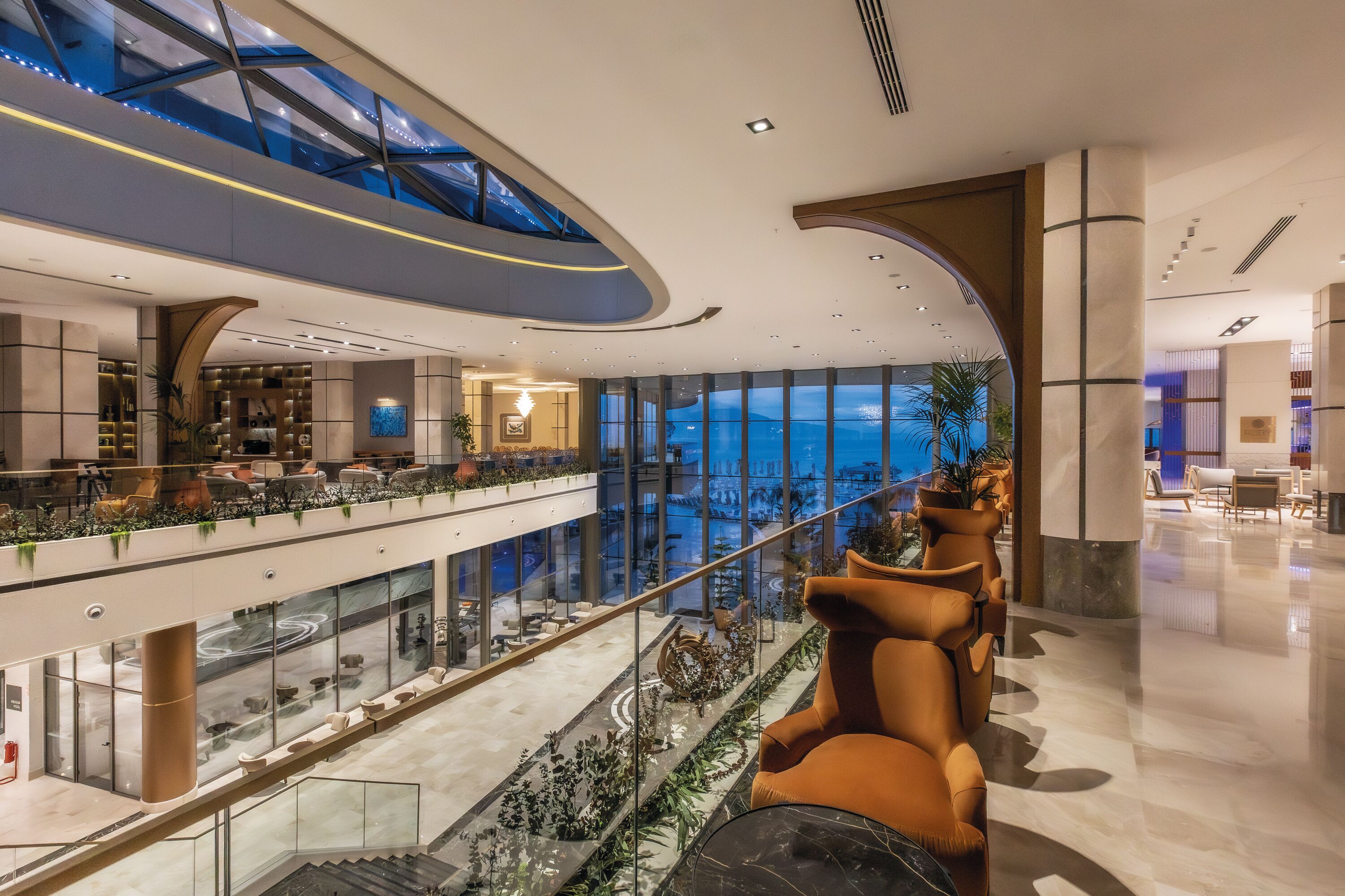 A modern hotel lobby with a glass atrium, seating areas, and a view of the outdoors.