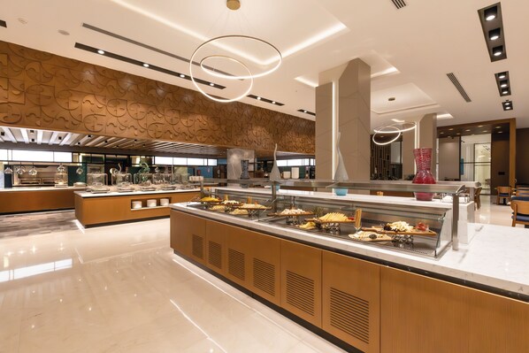 Un buffet moderne, typique des hôtels, avec un îlot central, un éclairage suspendu et un mur décoratif.