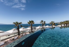 Una piscina infinita con vistas al mar, palmeras y sillones de descanso.