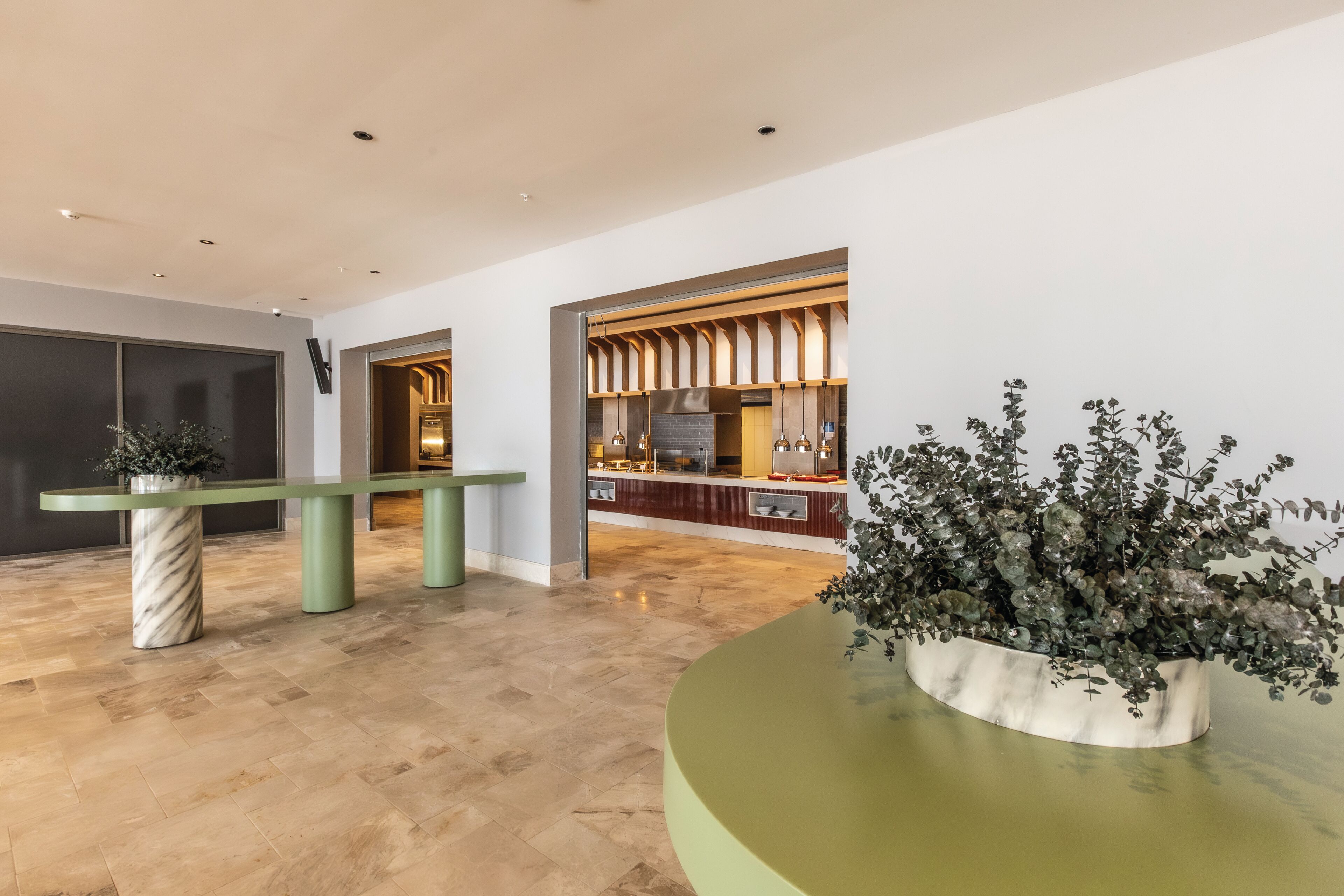 A modern lobby with a reception desk, a marble column, and a large potted plant.