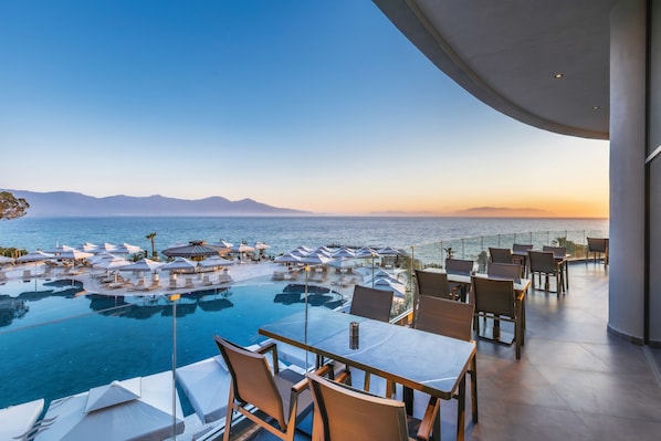 A poolside area with lounge chairs and umbrellas, overlooking a body of water and distant mountains.