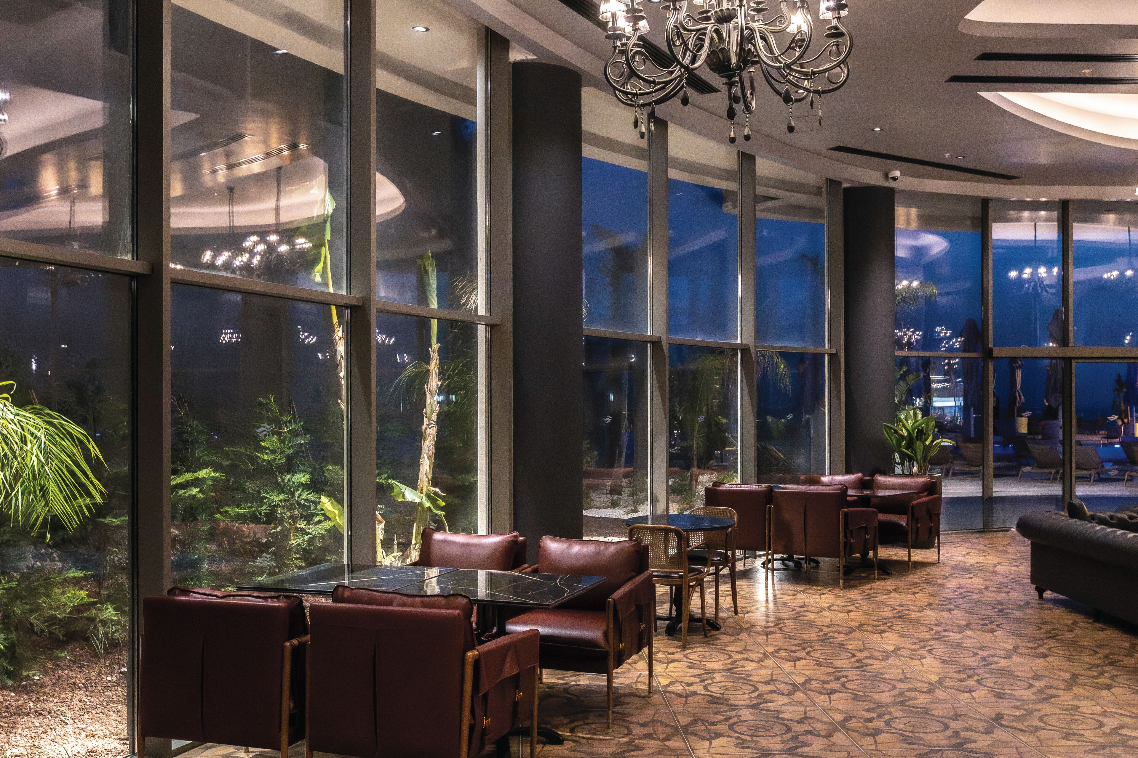 A spacious indoor area with large windows, leather seating, and a chandelier.