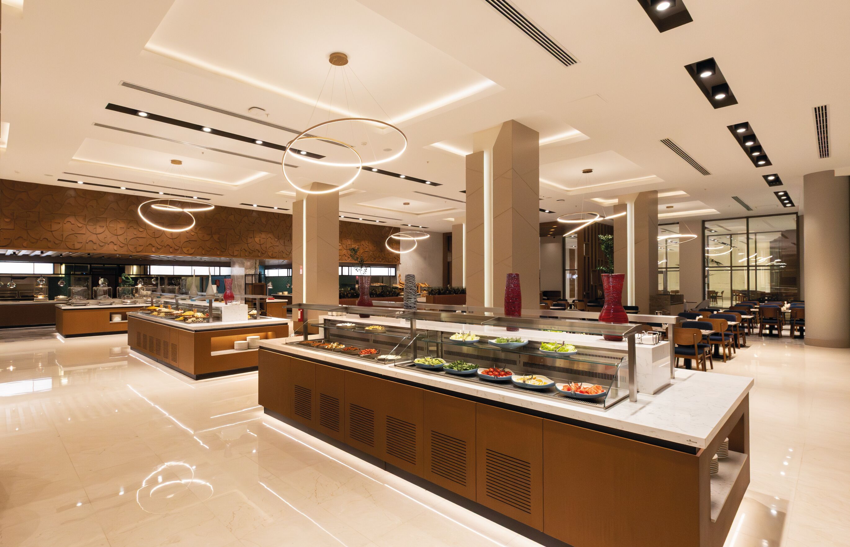 Un buffet moderne doté de plusieurs postes de service, d’un espace central où les plats sont présentés et d’un coin repas avec des tables et des chaises.