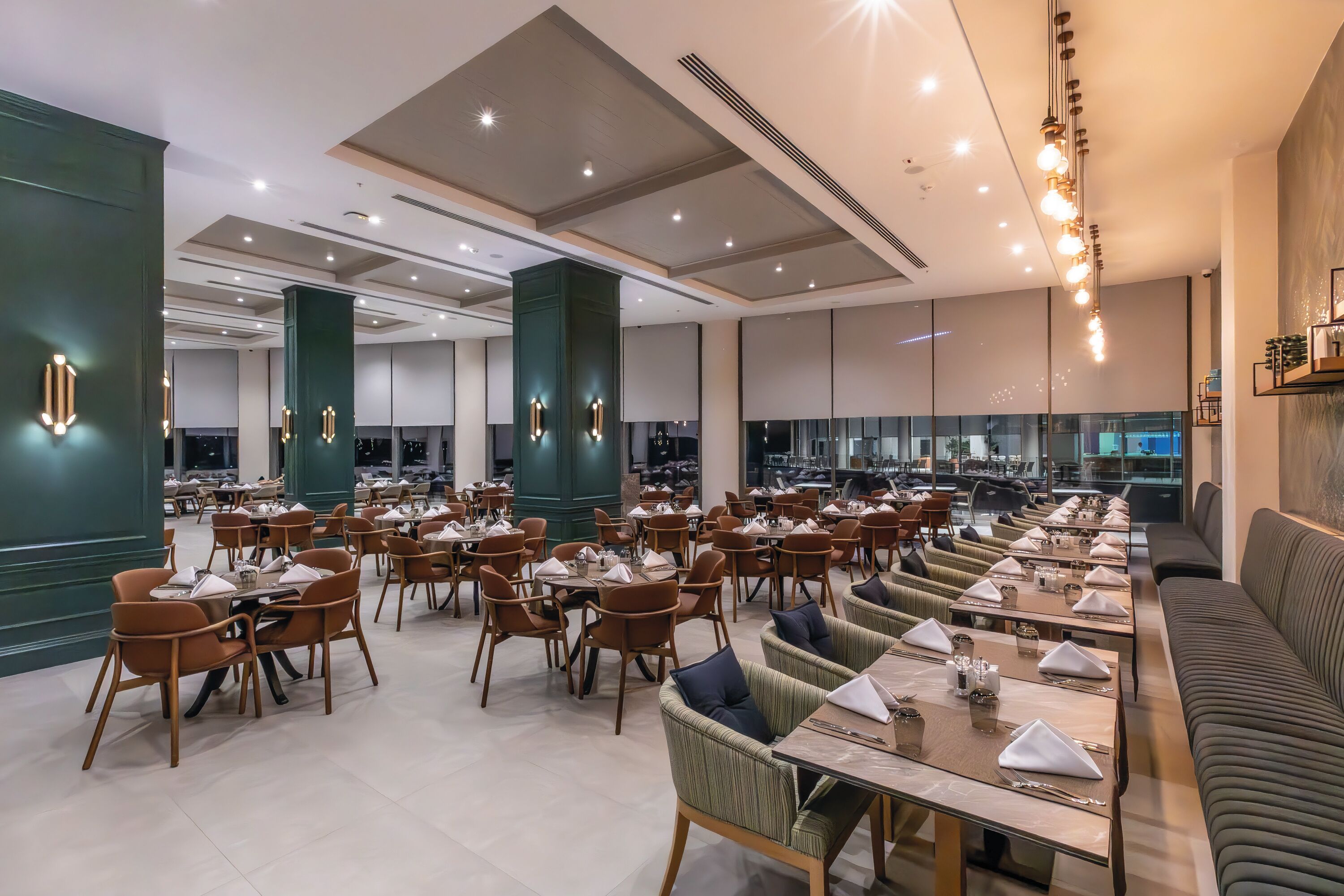 Un'ampia sala da pranzo con diversi tavoli e sedie, imponenti pilastri e un moderno design del soffitto.