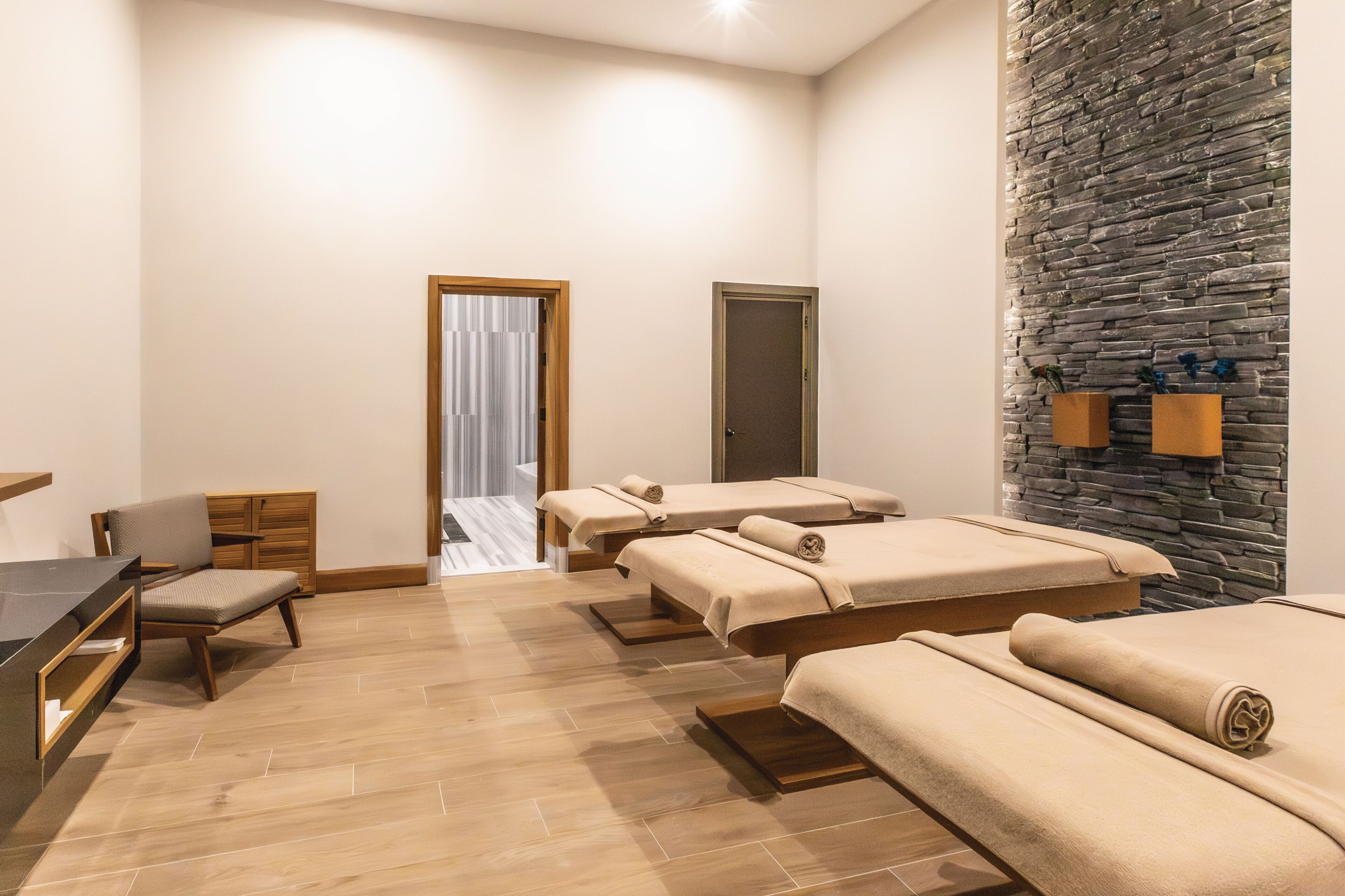 A spa room with three massage tables, a wooden desk, a chair, and a stone wall.