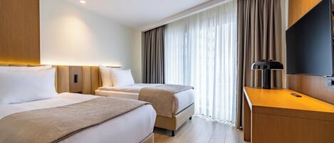 A hotel room with two beds, a desk, a flat-screen TV, and a large window with curtains.
