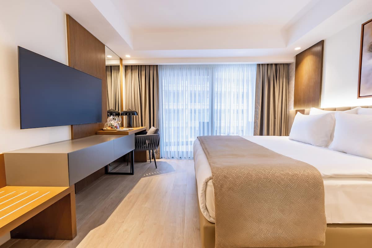 A modern hotel room with a bed, desk, and TV.