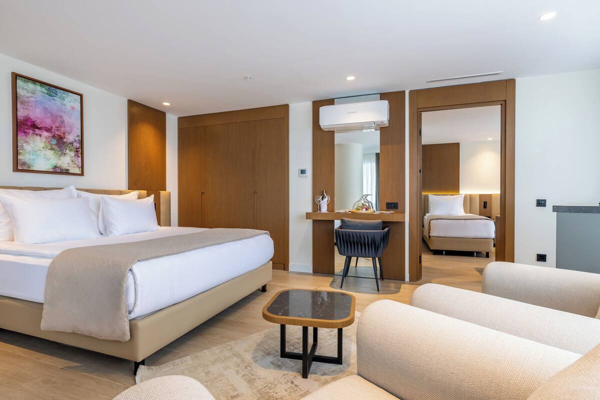 A modern hotel room with a large bed, a desk, a chair, and a sofa.