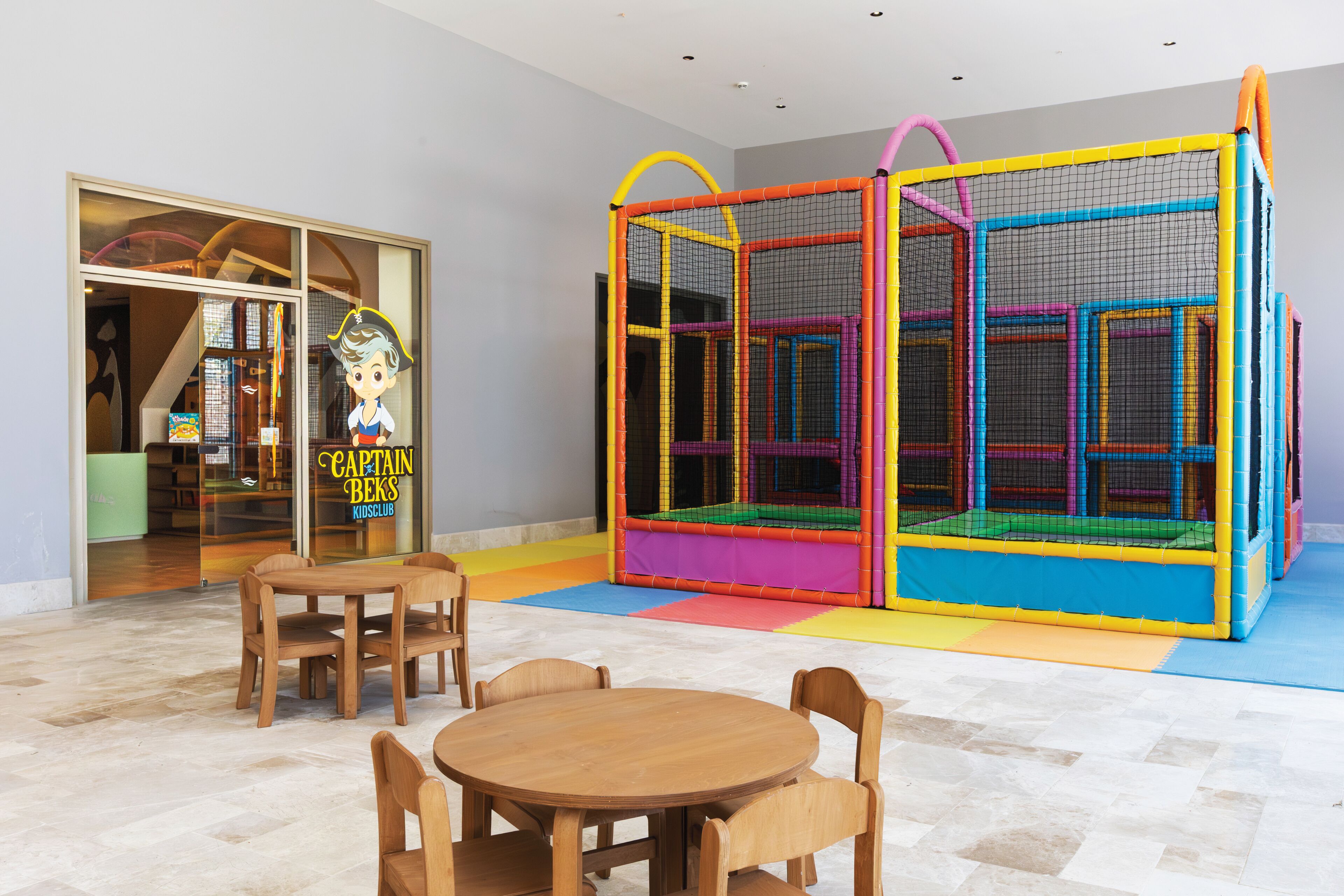 Un espace de jeux équipé d’une table et de chaises, d’une structure de jeux colorée et d’une entrée bien visible menant à un club pour enfants.