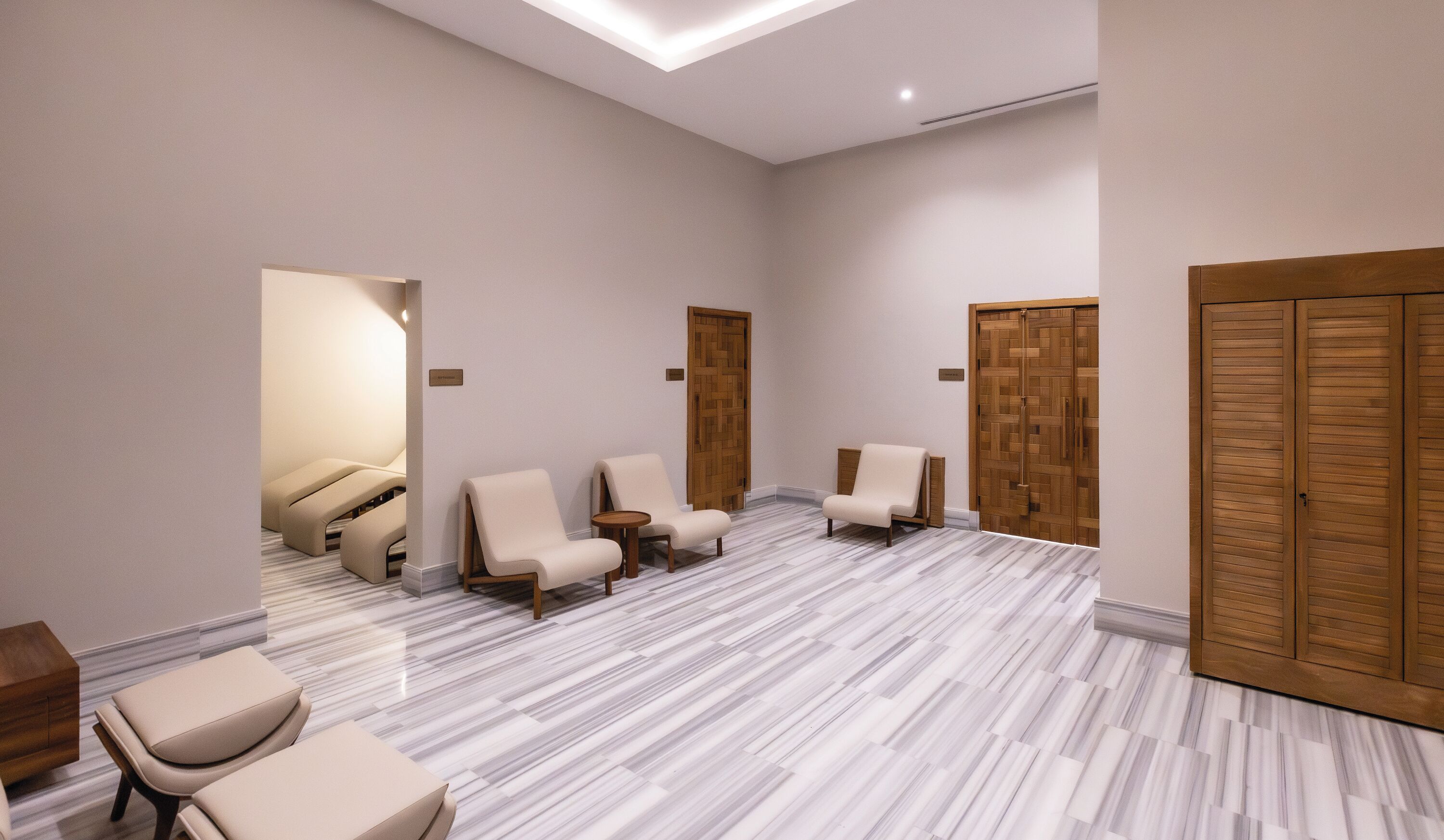 Quarto amplo com piso de mármore, portas de madeira e uma área de estar com cadeiras.