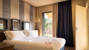 Une chambre d’hôtel avec un lit, une table de chevet en bois, un luminaire suspendu et une porte donnant sur un balcon.