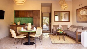 Un vaste espace de vie comprenant une table à manger, des chaises en osier, un canapé et une cuisine dotée de meubles en bois et d’un plan de travail vert.