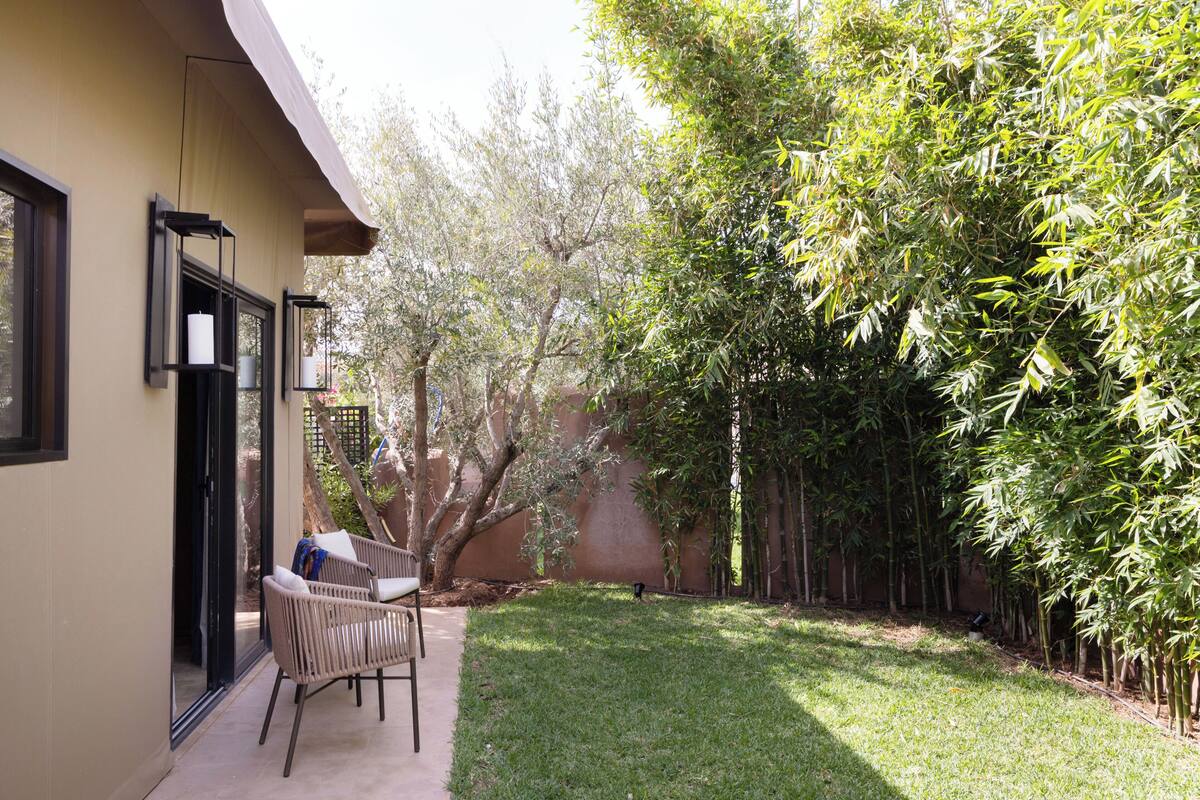 A patio with a wicker chair and a table, a small tree, and a bamboo fence.