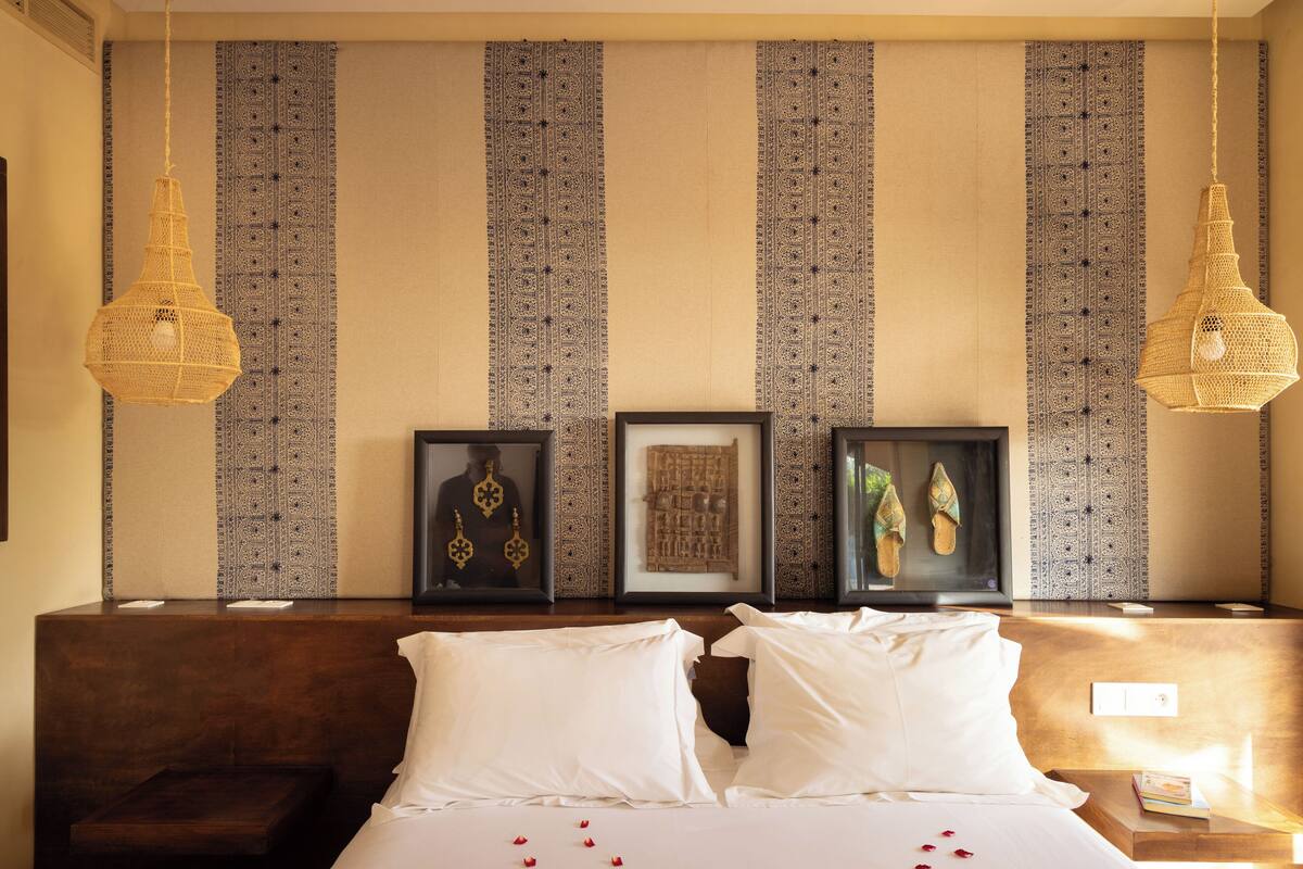 A hotel room with a large bed, two hanging lamps, and a wall with patterned wallpaper.