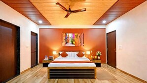Una habitación de hotel con techo de madera, una cama grande con cabecera, un cuadro en la pared y un ventilador de techo.