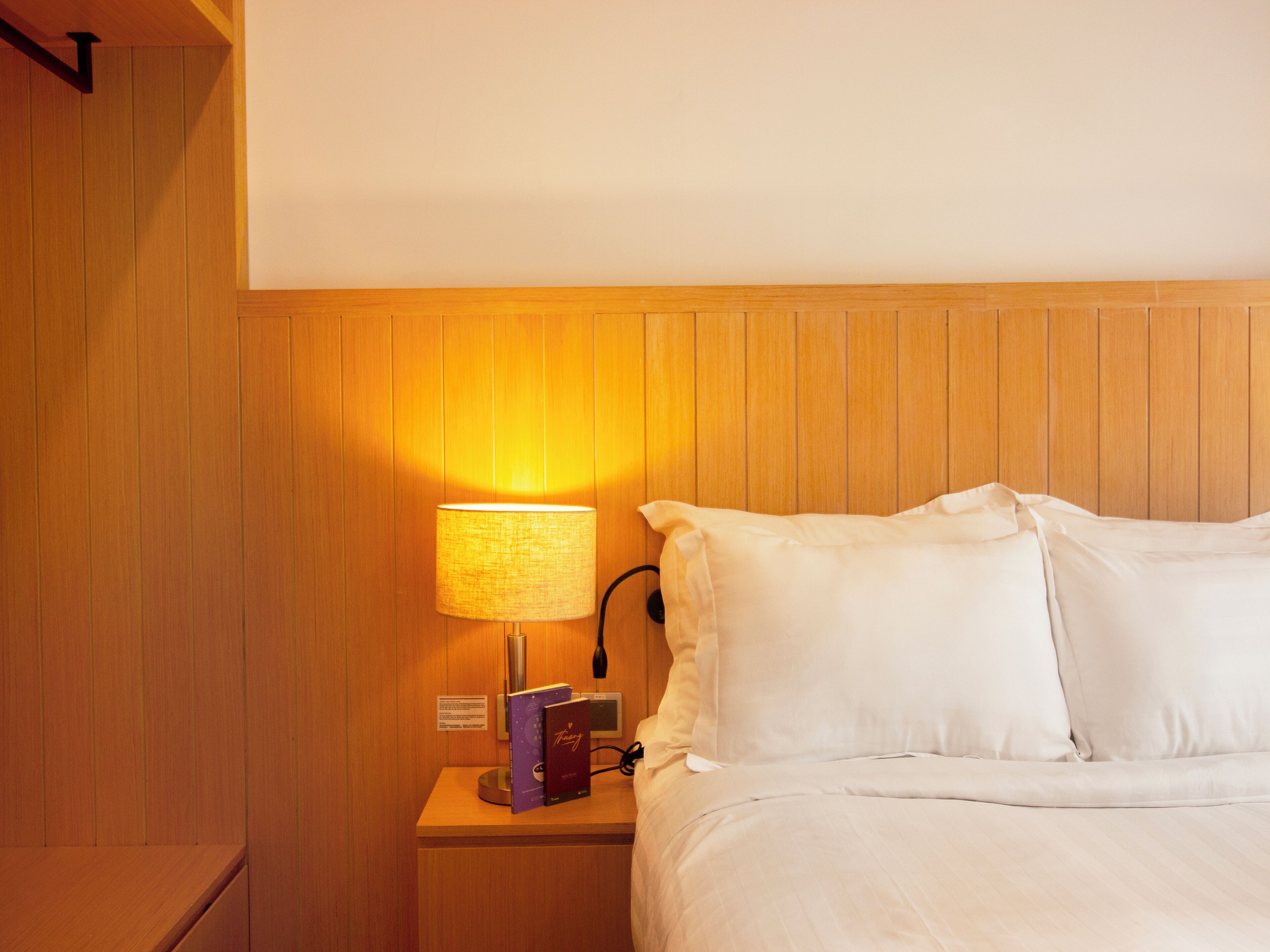 Une chambre d’hôtel avec une tête de lit en bois, une table de chevet avec une lampe, des livres et un lit soigneusement fait.