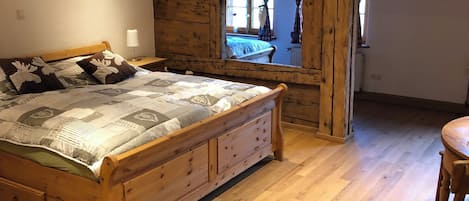 A wooden bed with storage drawers, a wooden chair, and a window with curtains.