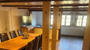Uma mesa de jantar de madeira com cadeiras, uma televisão e uma janela com cortinas.