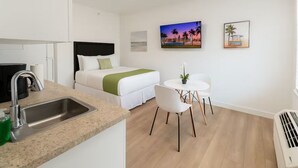 Una habitación de hotel moderna con una cama, una pequeña mesa de comedor, un lavamanos y una sola silla.