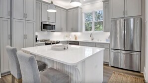 Una cocina moderna con armarios blancos, electrodomésticos de acero inoxidable e iluminación colgante.