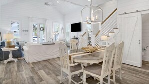 Una sala de estar amplia con un sofá blanco, una mesa de comedor con sillas blancas y una escalera con baranda de madera.